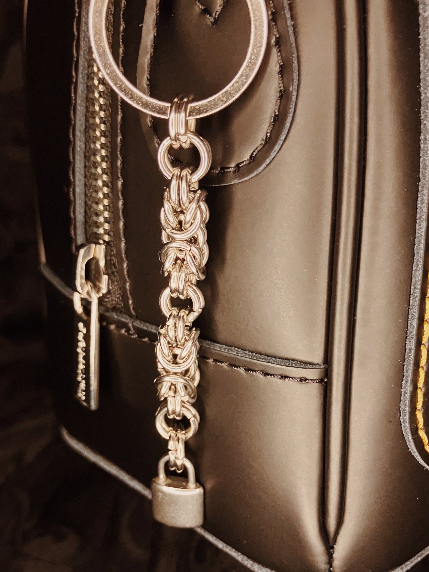 Silver chain keychain with padlock attached to a black leather bag.