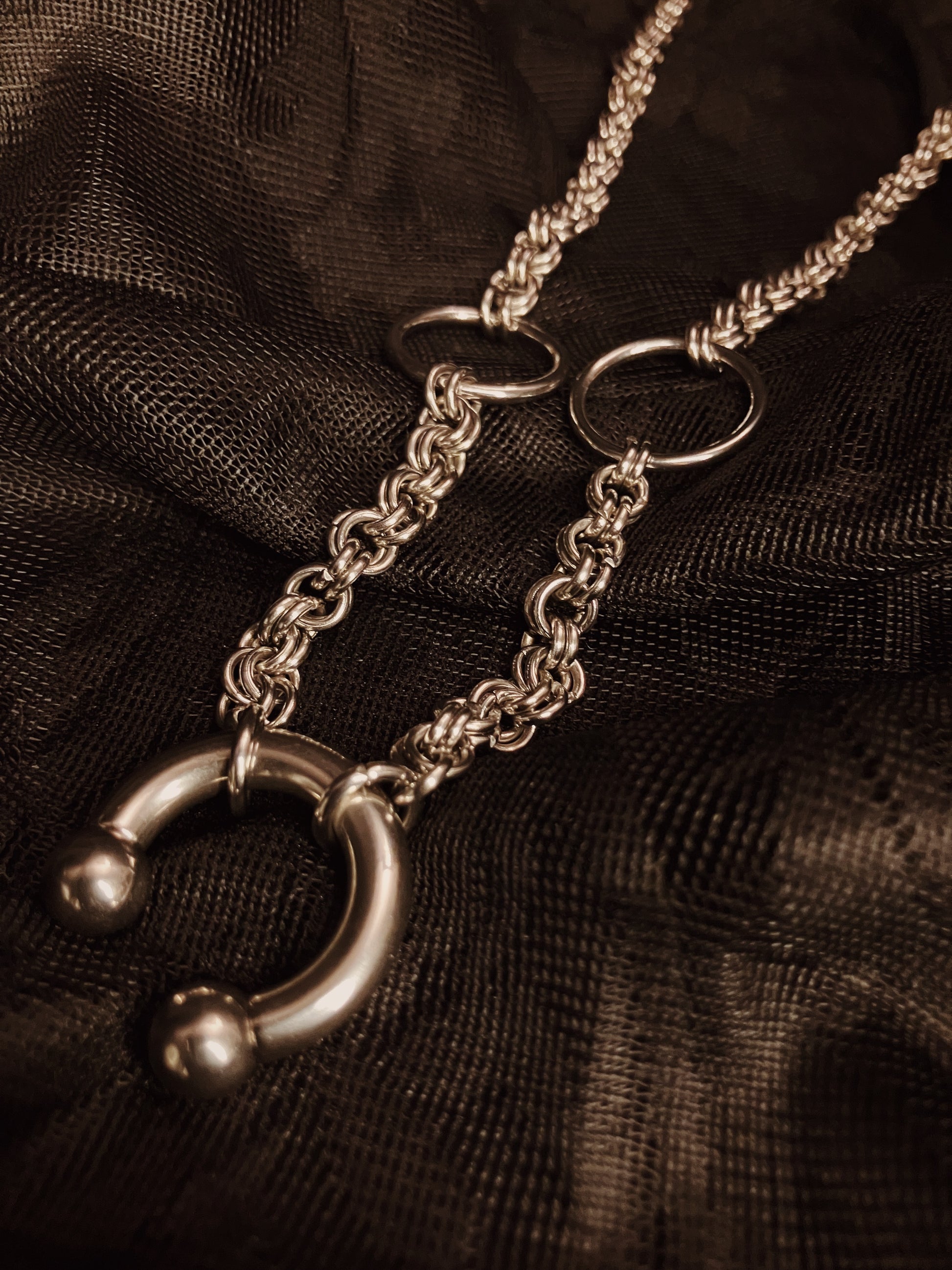 Silver chain necklace with a unique clasp on a dark fabric background