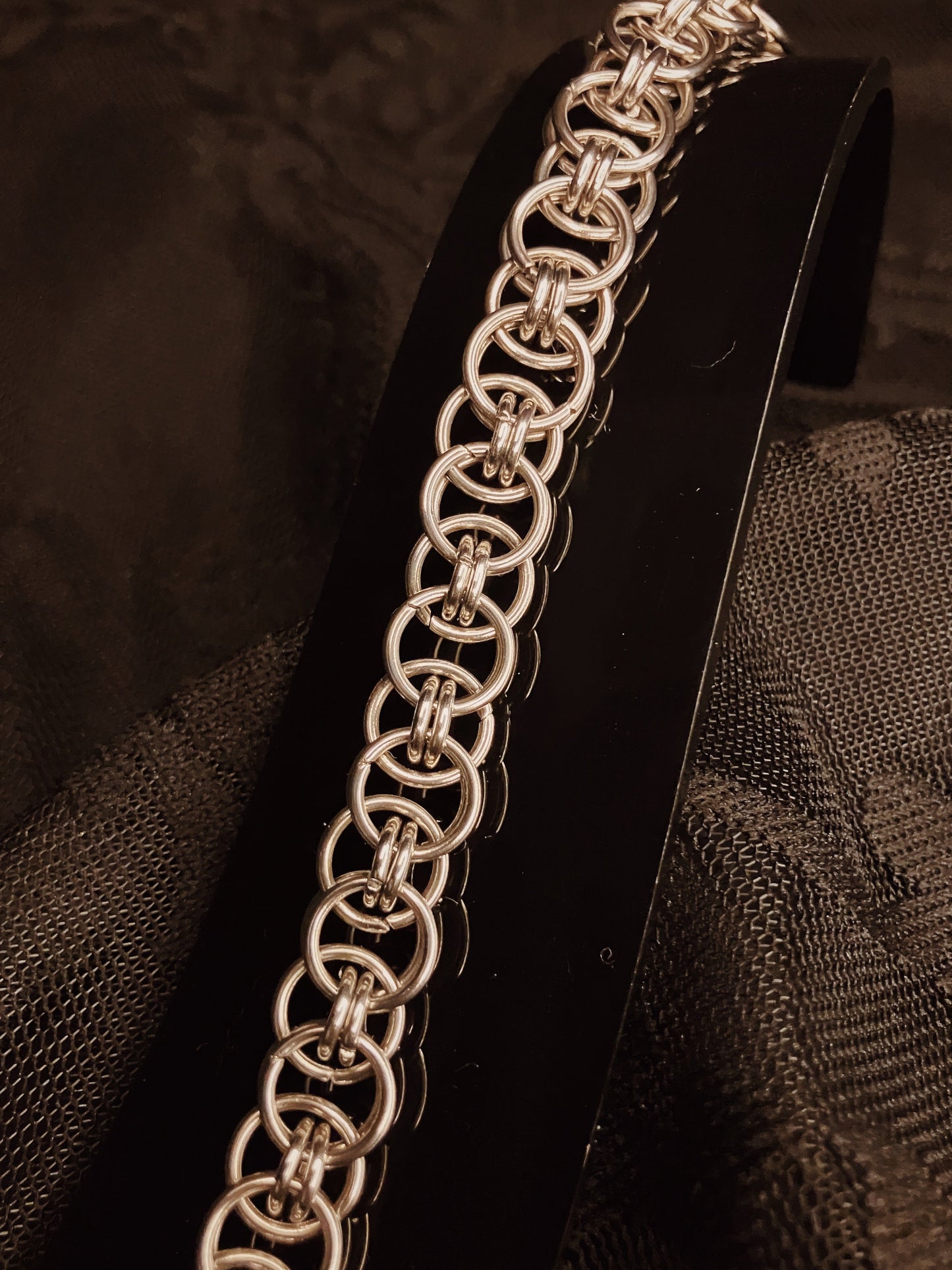 Silver chain bracelet on a black stand against a textured brown background