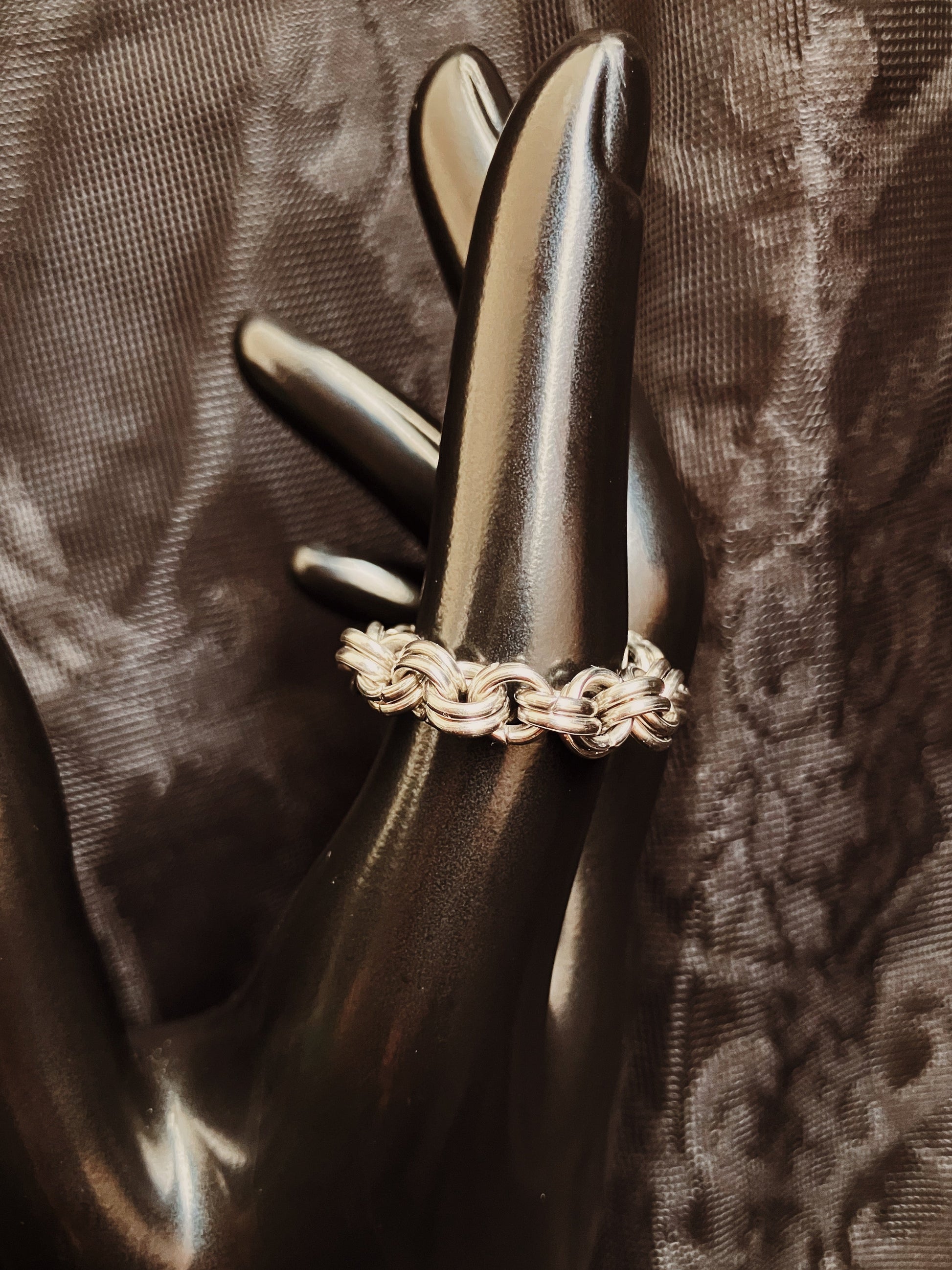 Silver ring with a chain design on a dark textured fabric background