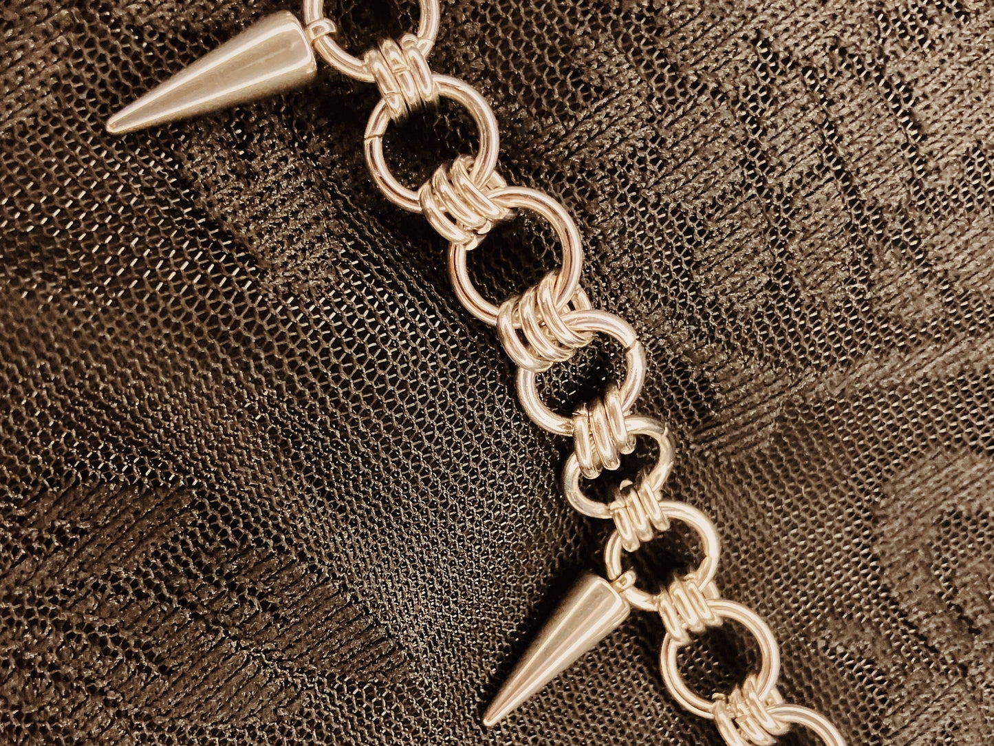 Silver chain bracelet with spike-like ends on a textured brown background