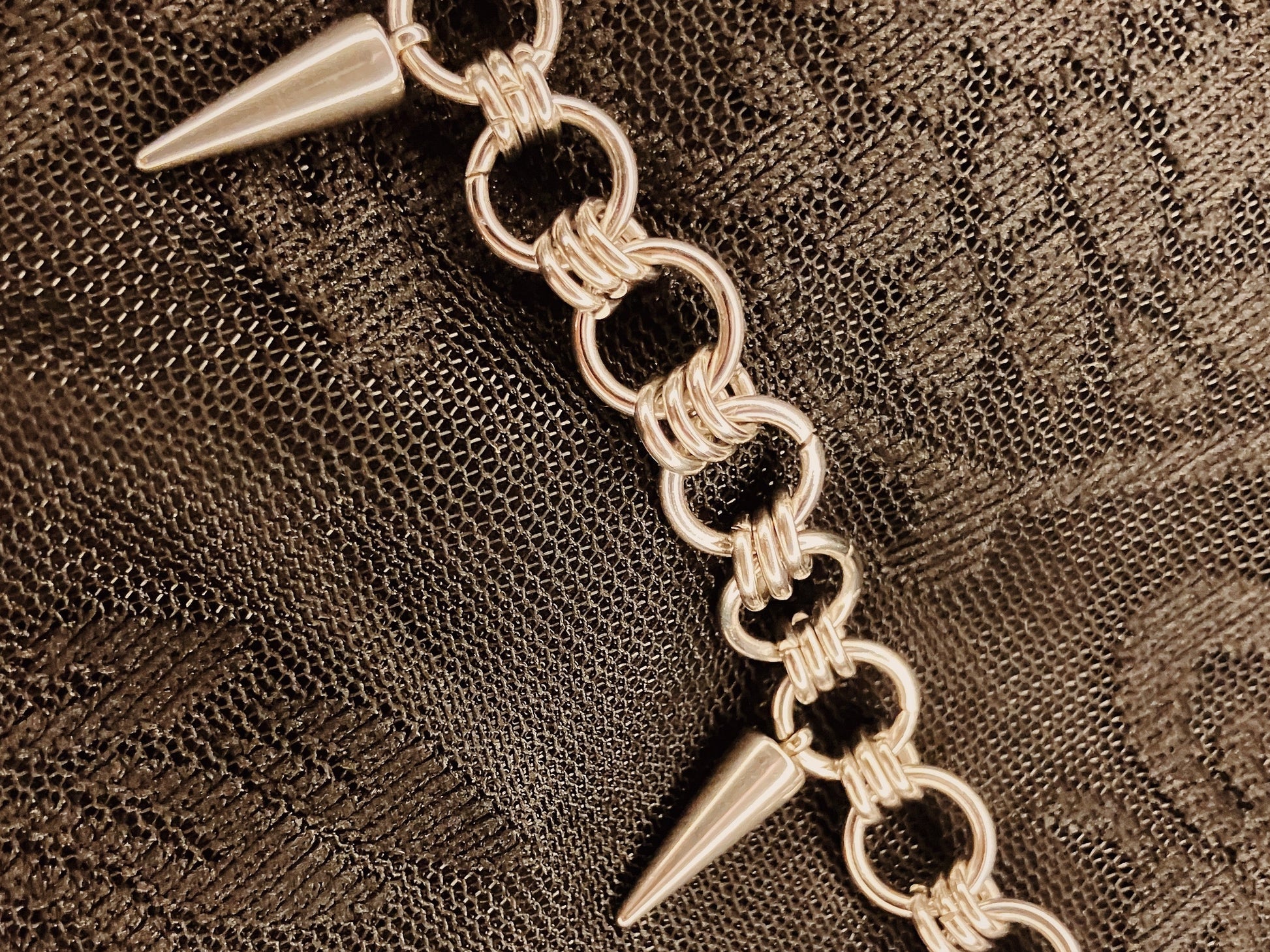 Silver chain bracelet with spike-like ends on a textured brown background