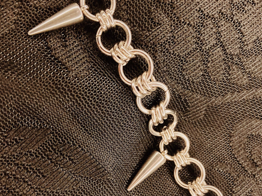 Silver chain bracelet with spike-like ends on a textured brown background