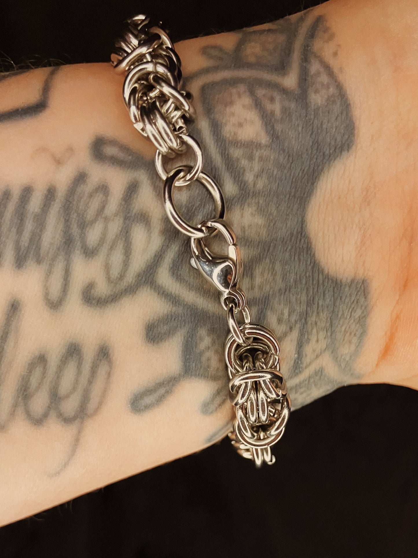 Silver chain bracelet with a unique clasp on a tattooed arm.