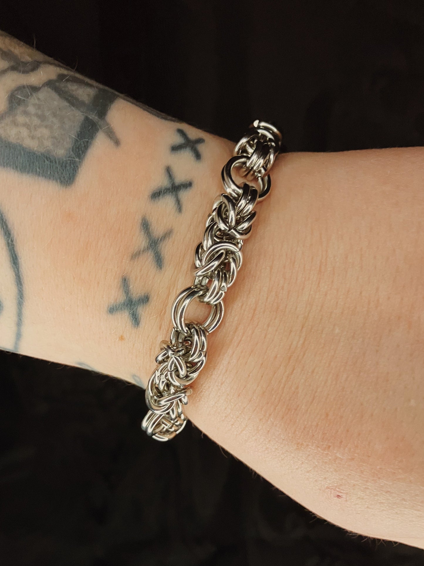 Silver chain bracelet on a wrist with tattoos against a black background