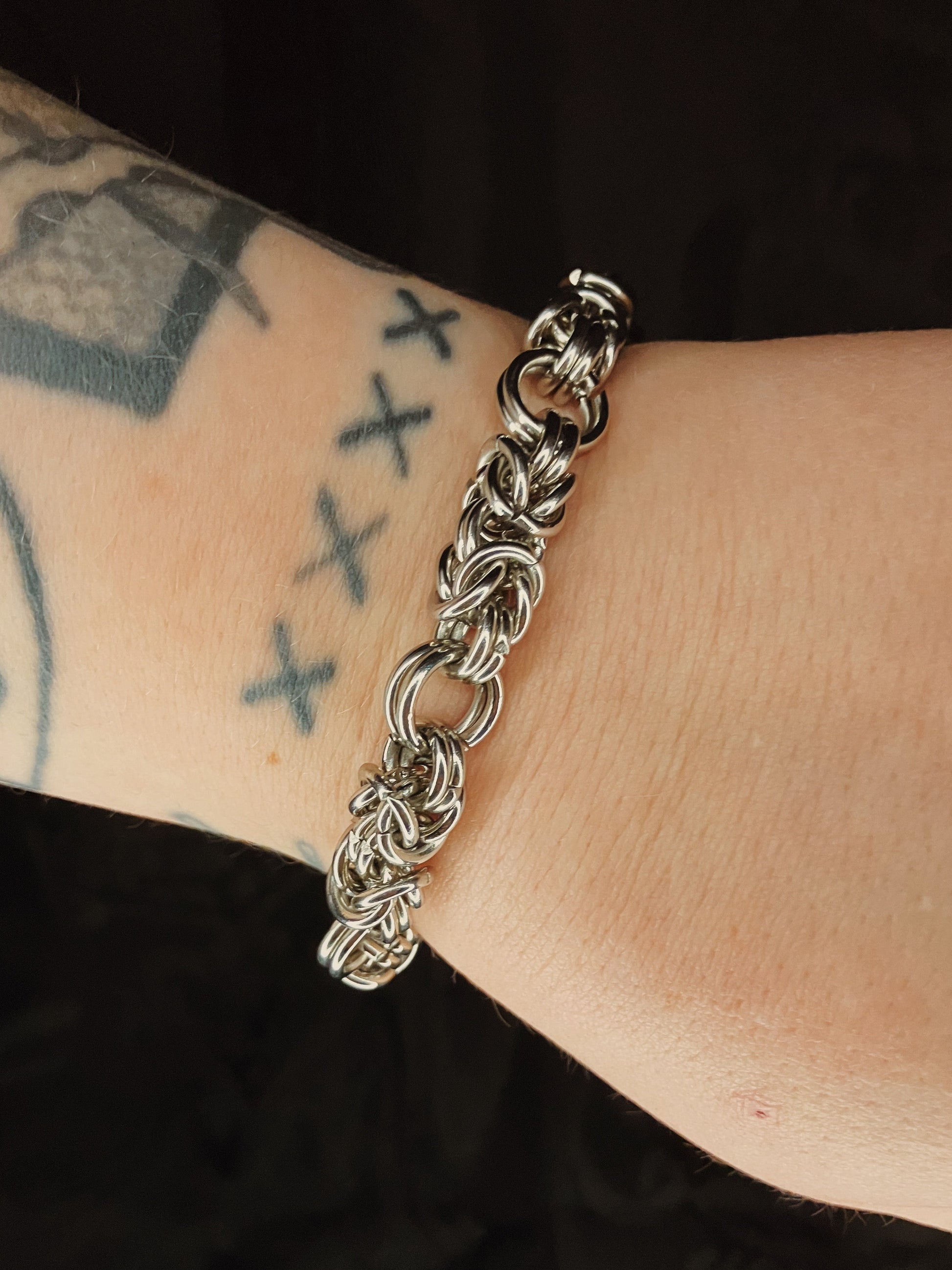Silver chain bracelet on a wrist with tattoos against a black background