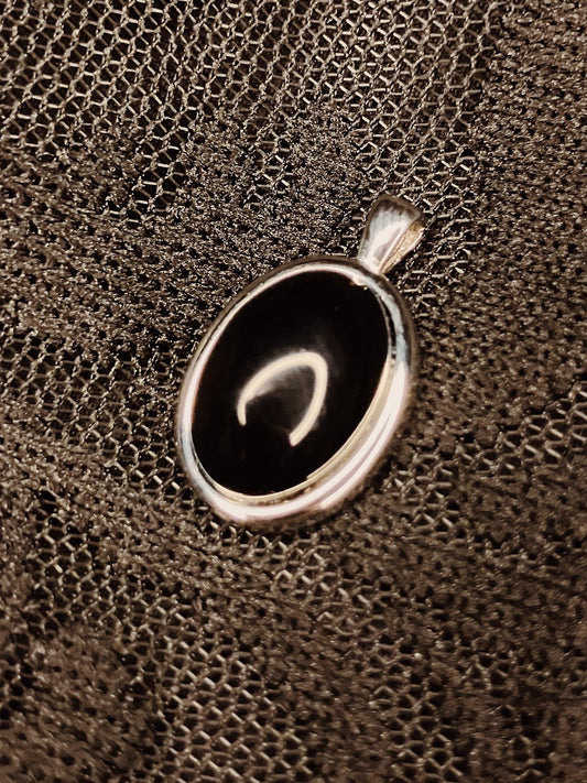 Silver pendant with a black stone on a textured brown surface