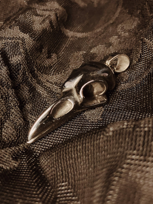 Metallic bird skull pendant on a textured fabric background