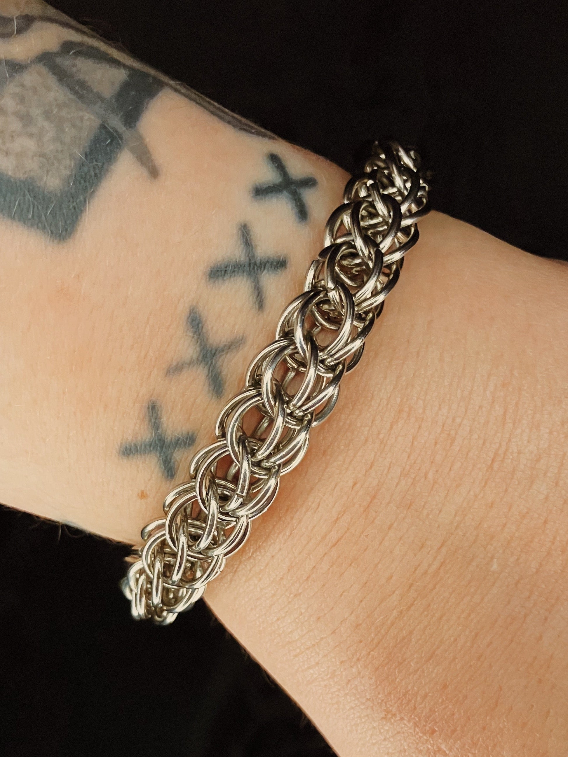 Silver chain bracelet on a wrist with tattoos