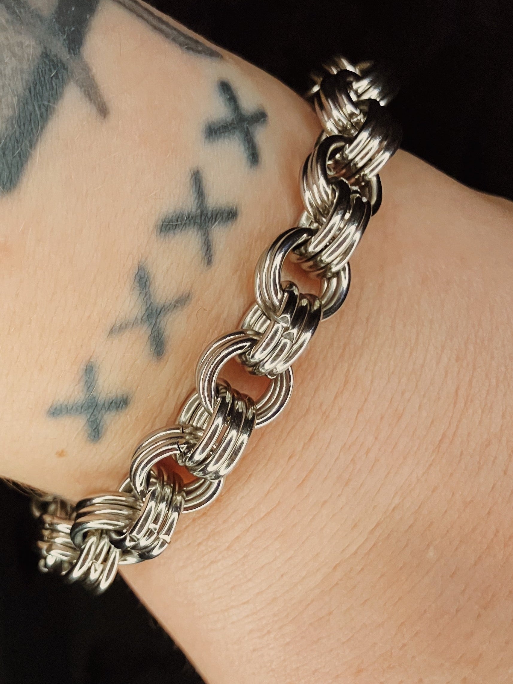 Silver chain bracelet on a wrist with tattoos