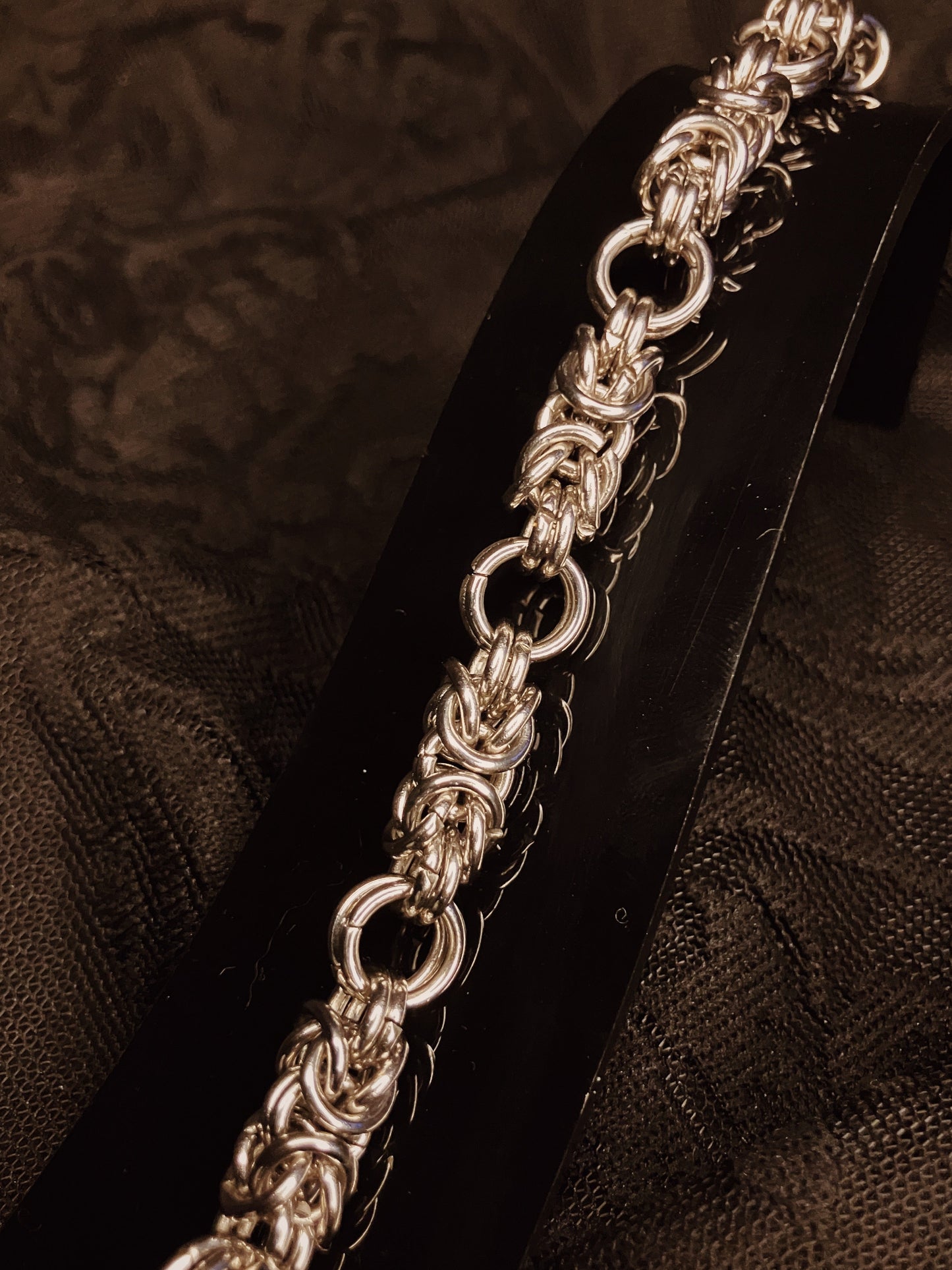 Silver chain bracelet on a black stand against a textured brown background