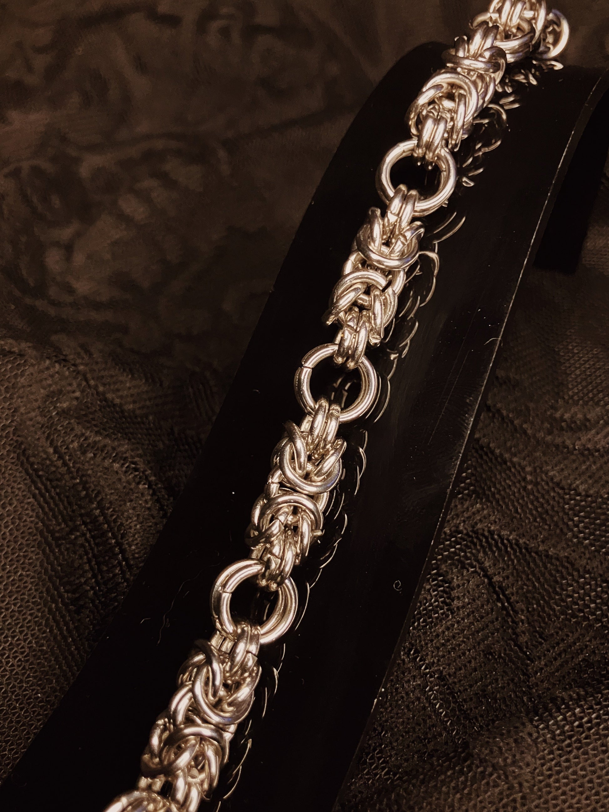 Silver chain bracelet on a black stand against a textured brown background