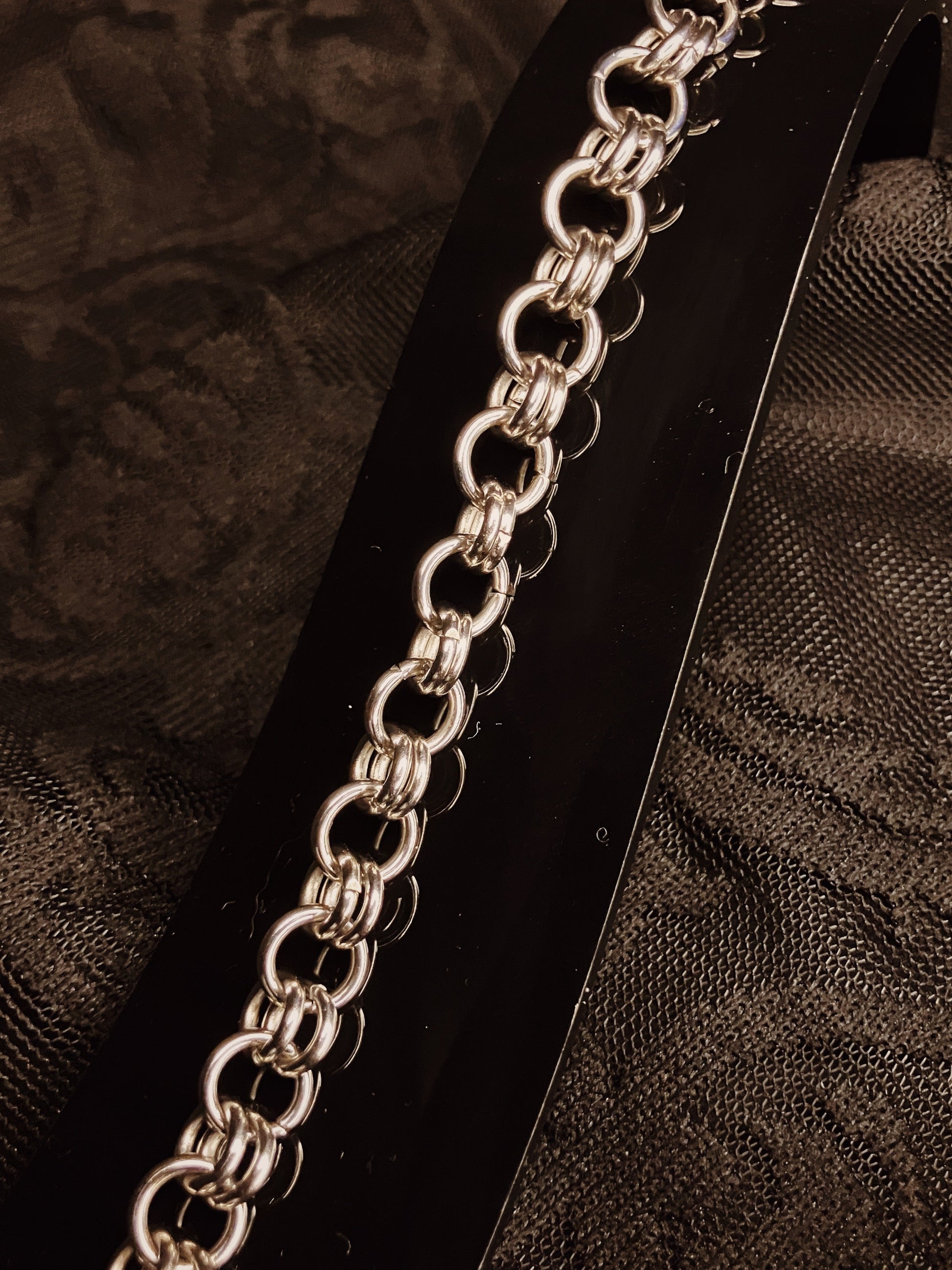 Silver chain bracelet on a black stand with a dark textured background