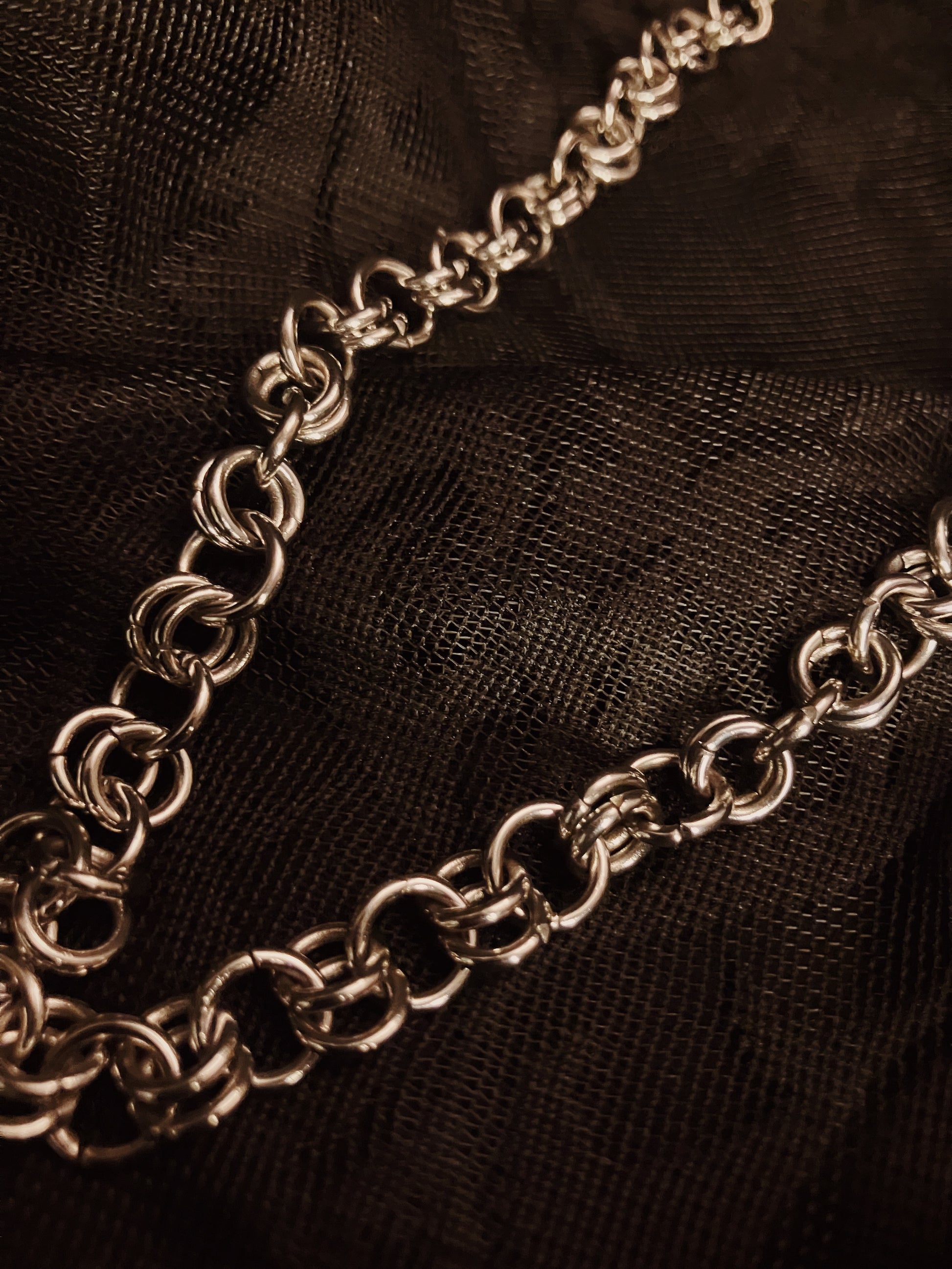 Silver chain necklace on a black textured fabric background