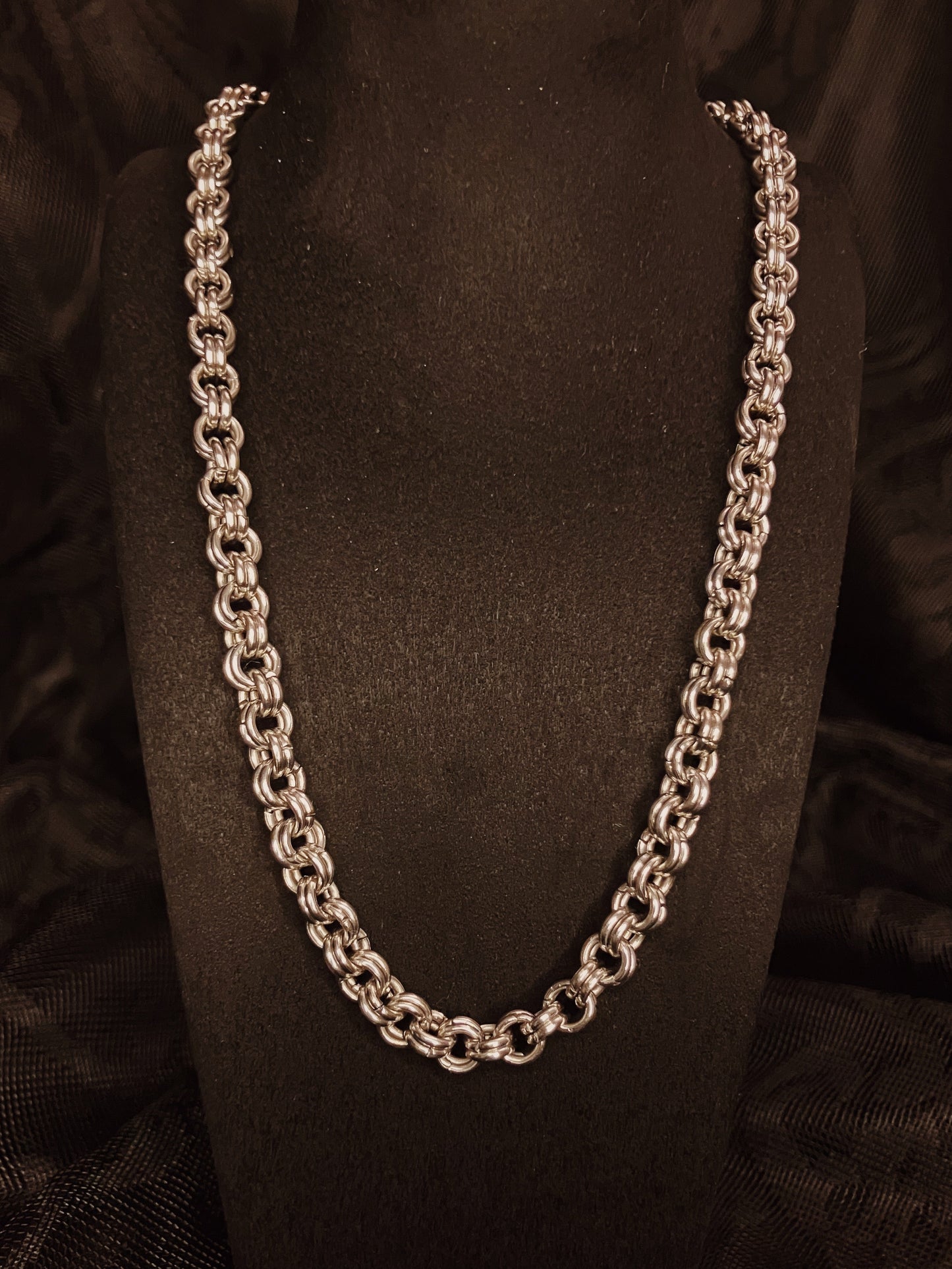 Silver chain necklace on a black stand with a black background