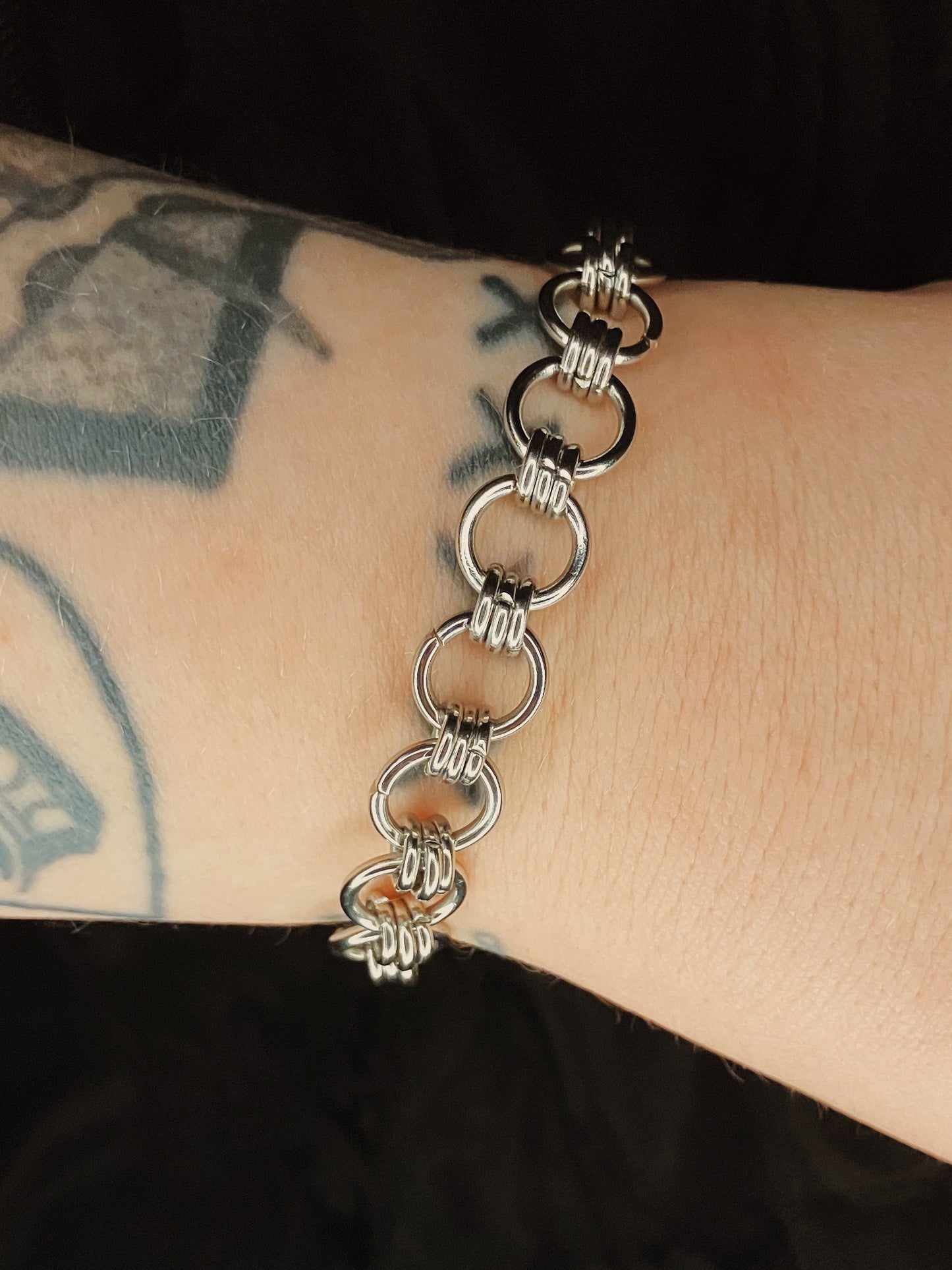 Silver chain bracelet on a wrist with tattoos