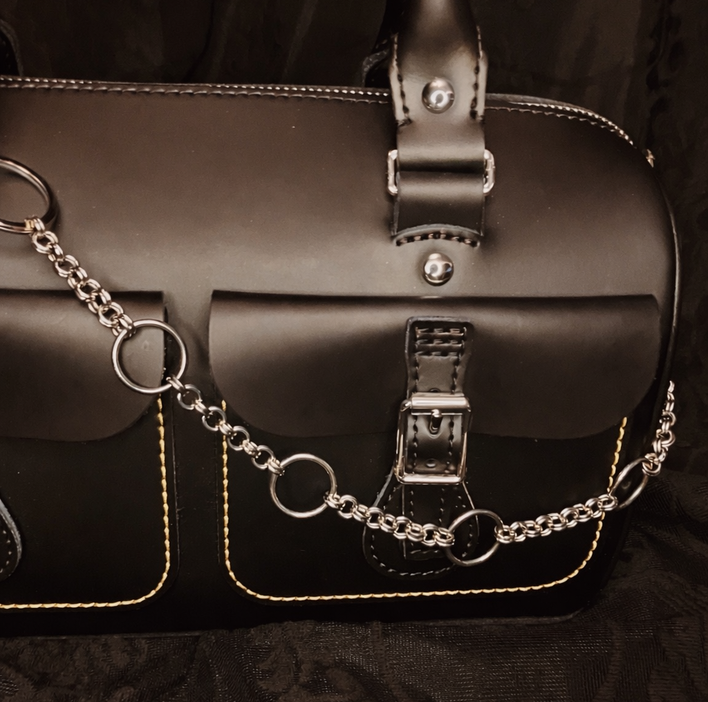 Black leather satchel with chain detail on a black textured background