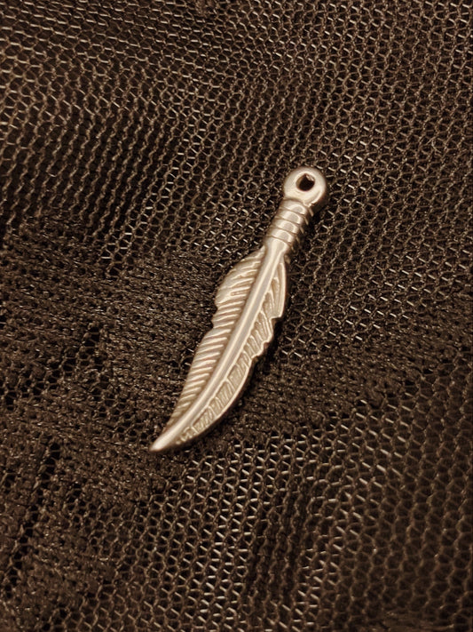 Silver feather-shaped pendant on a textured brown leather surface