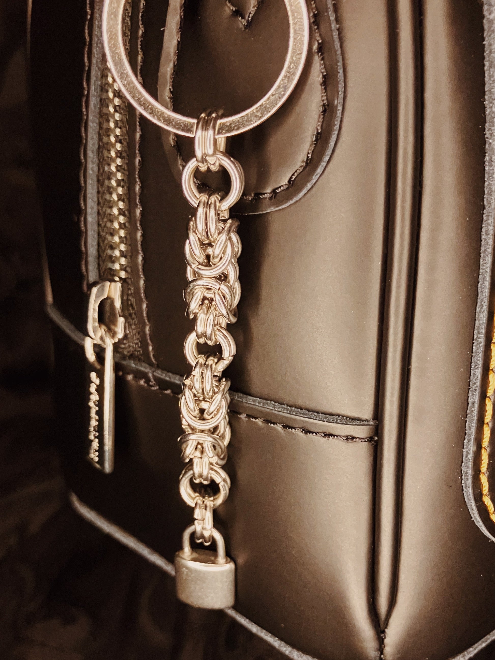 Silver chain keychain with padlock attached to a black leather bag.