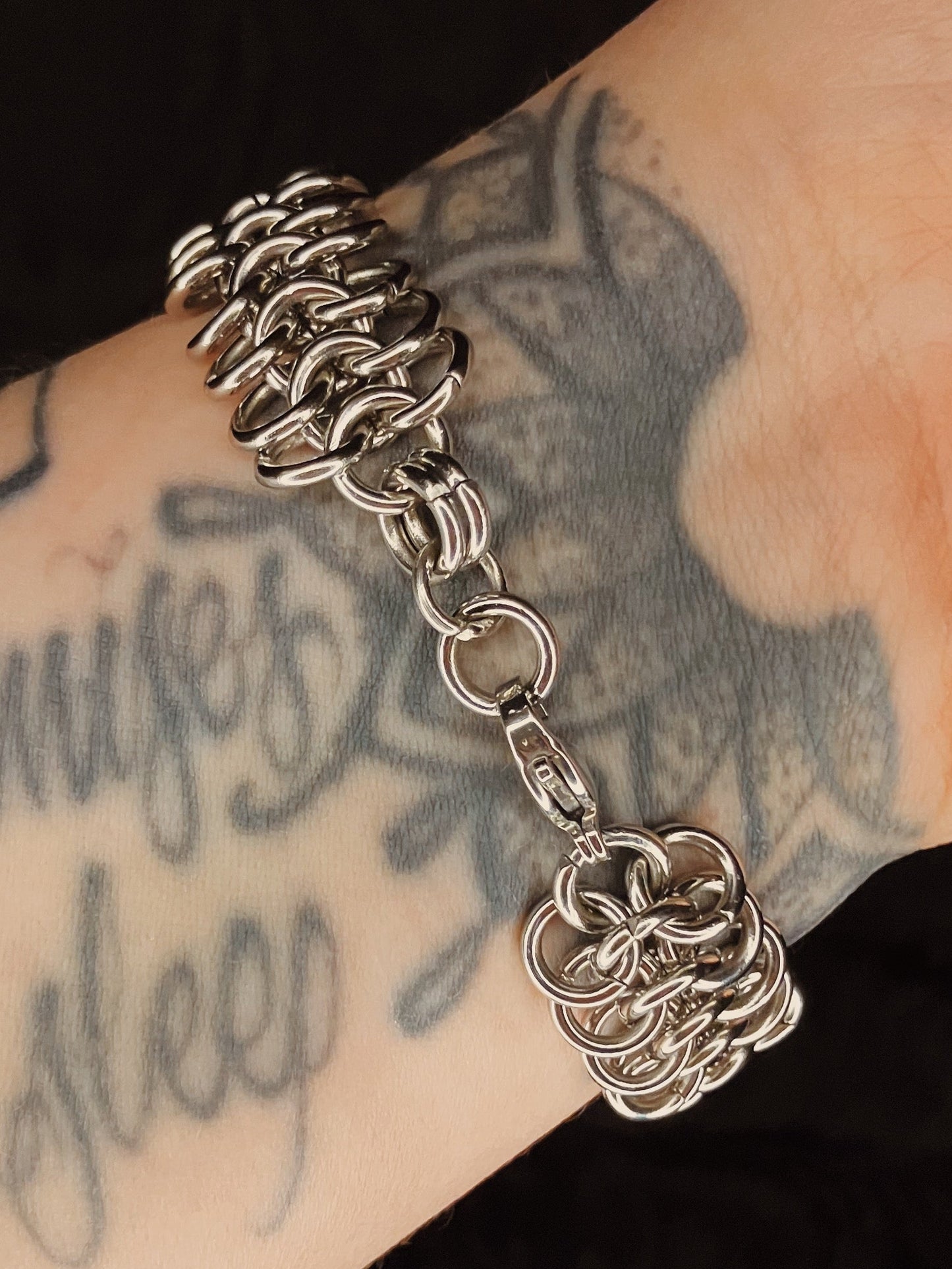 Silver chain bracelet on a tattooed arm.