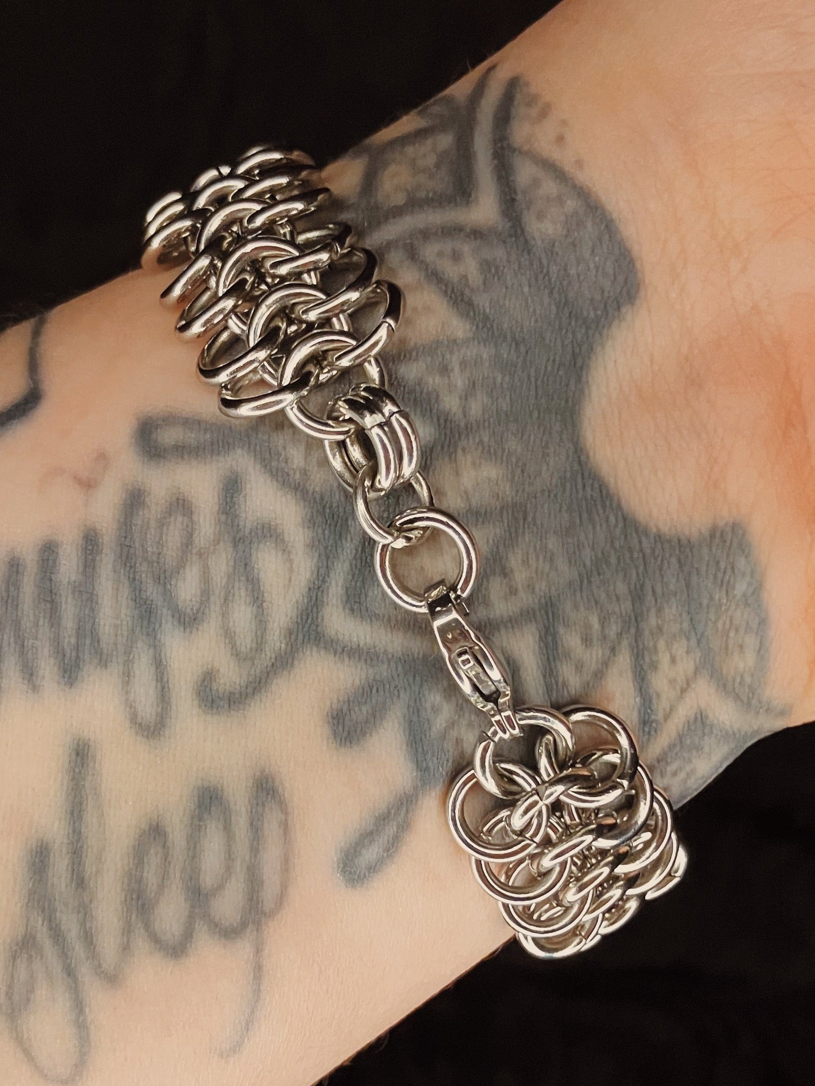 Silver chain bracelet on a tattooed arm.