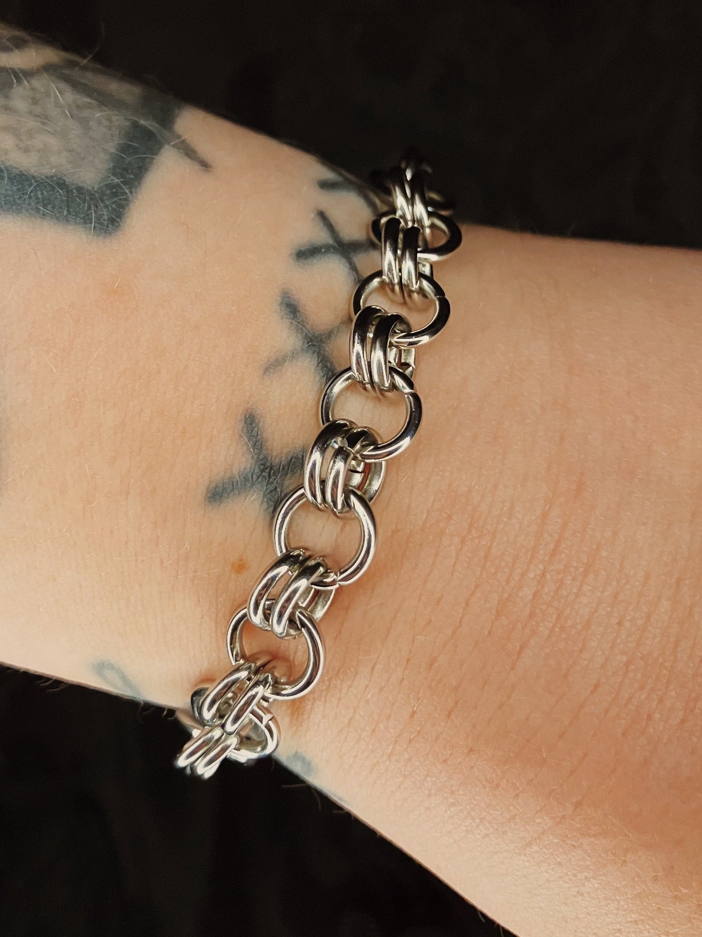 Silver chain bracelet on a wrist with tattoos