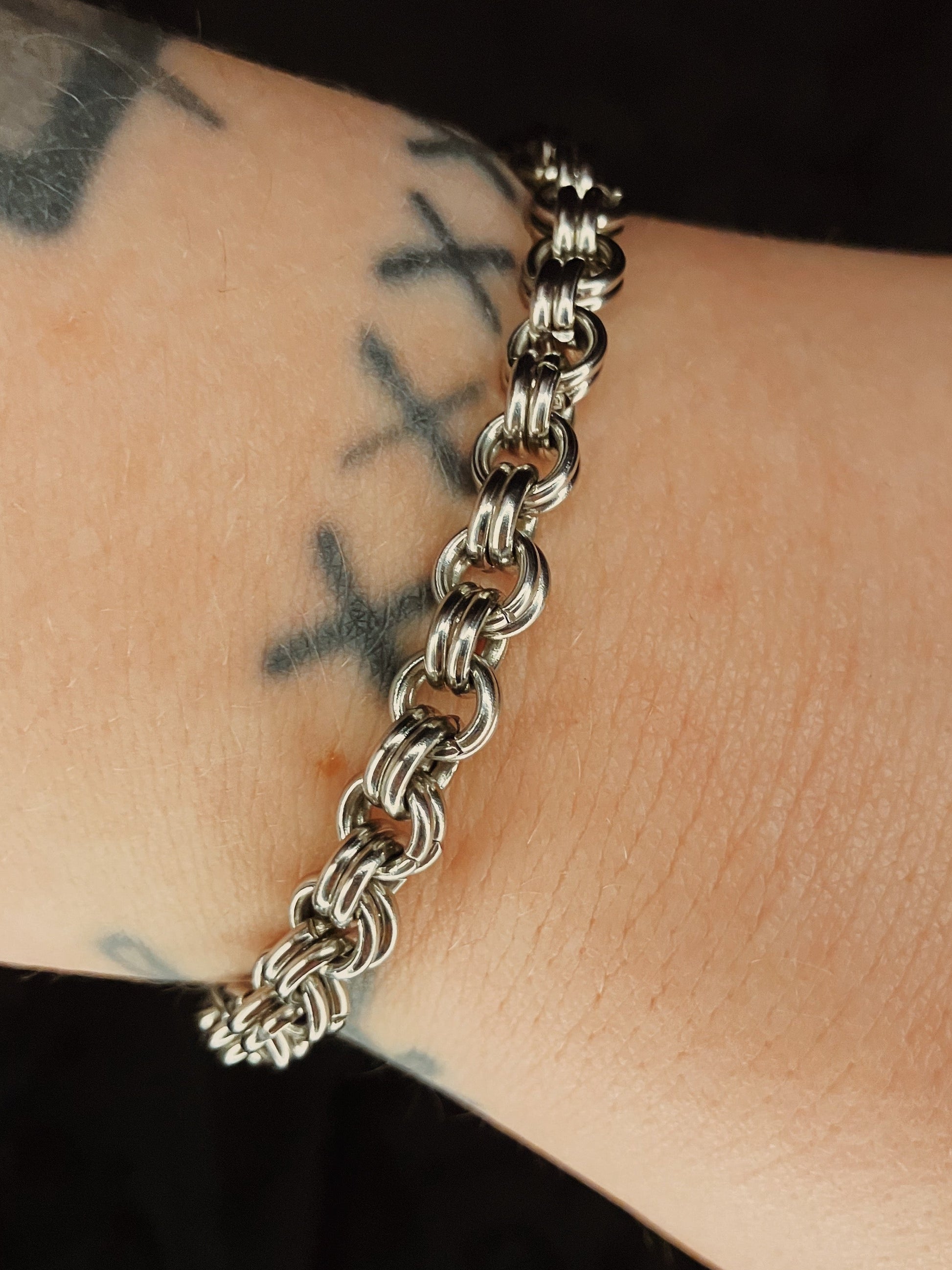 Silver chain bracelet on a wrist with tattoos