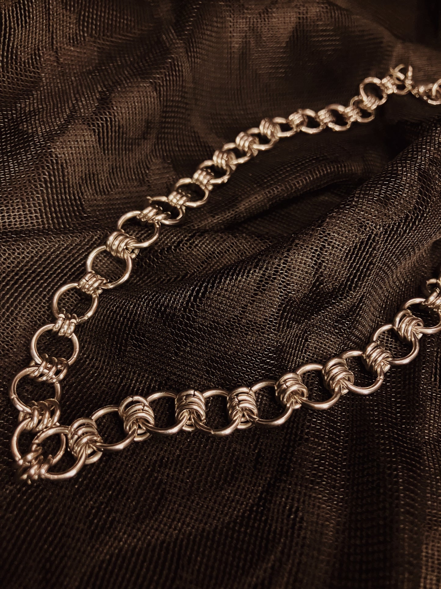 Silver chain necklace on a black textured fabric background