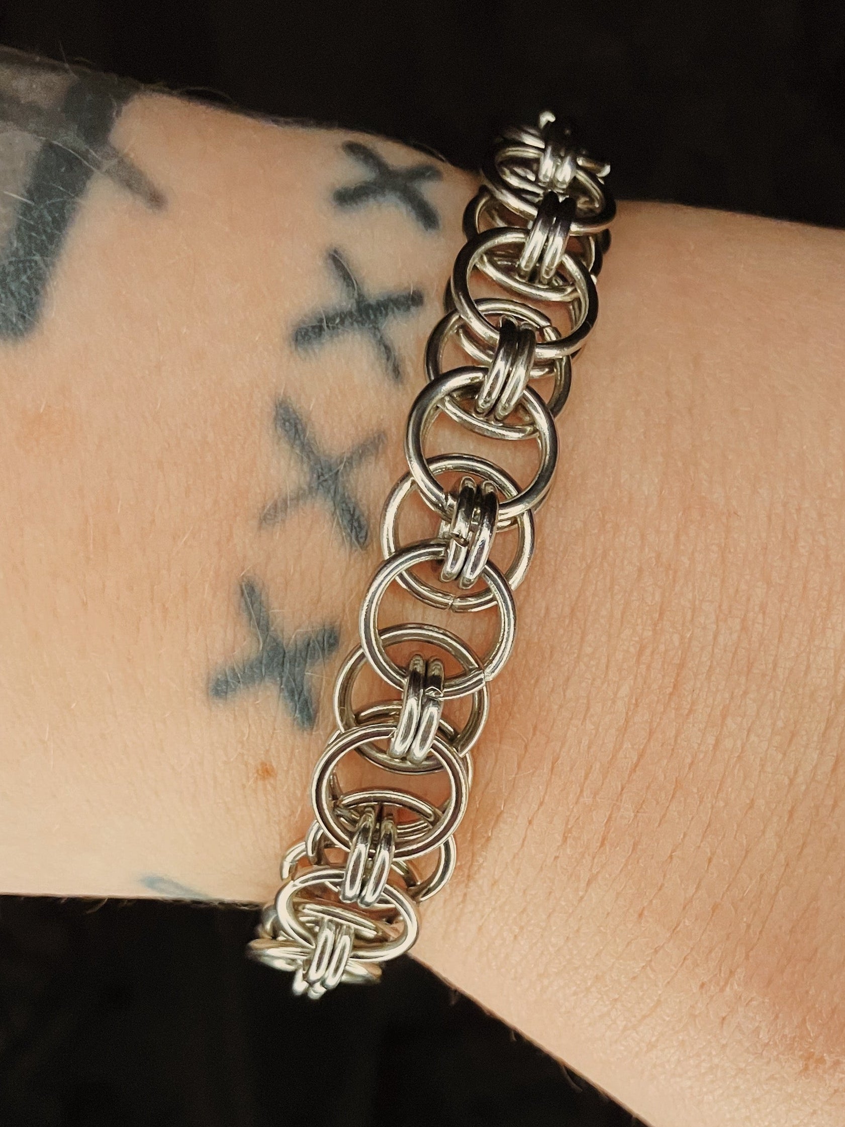 Silver chain bracelet on a wrist with tattoos