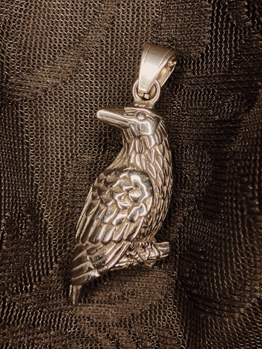 Silver bird-shaped pendant on a textured brown fabric background