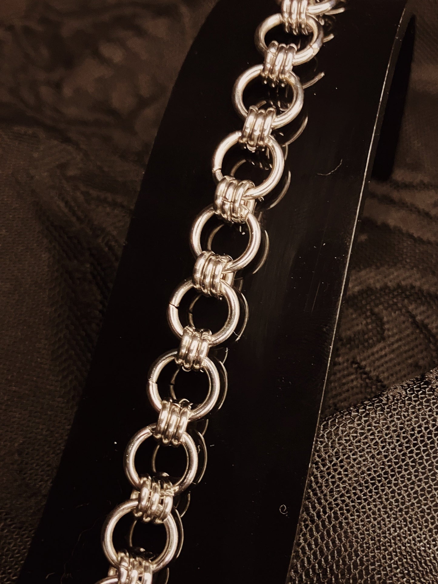 Silver chain bracelet on a black stand with a textured brown background
