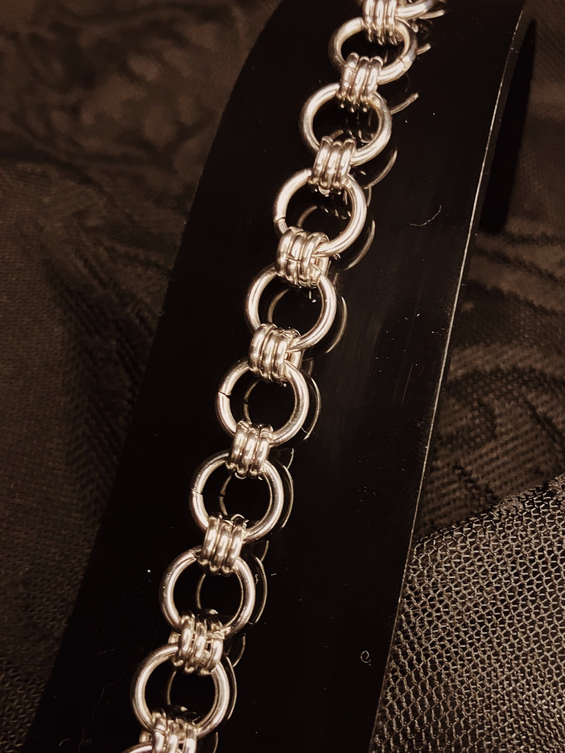 Silver chain bracelet on a black stand with a textured brown background