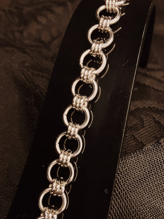 Silver chain bracelet on a black stand with a textured brown background