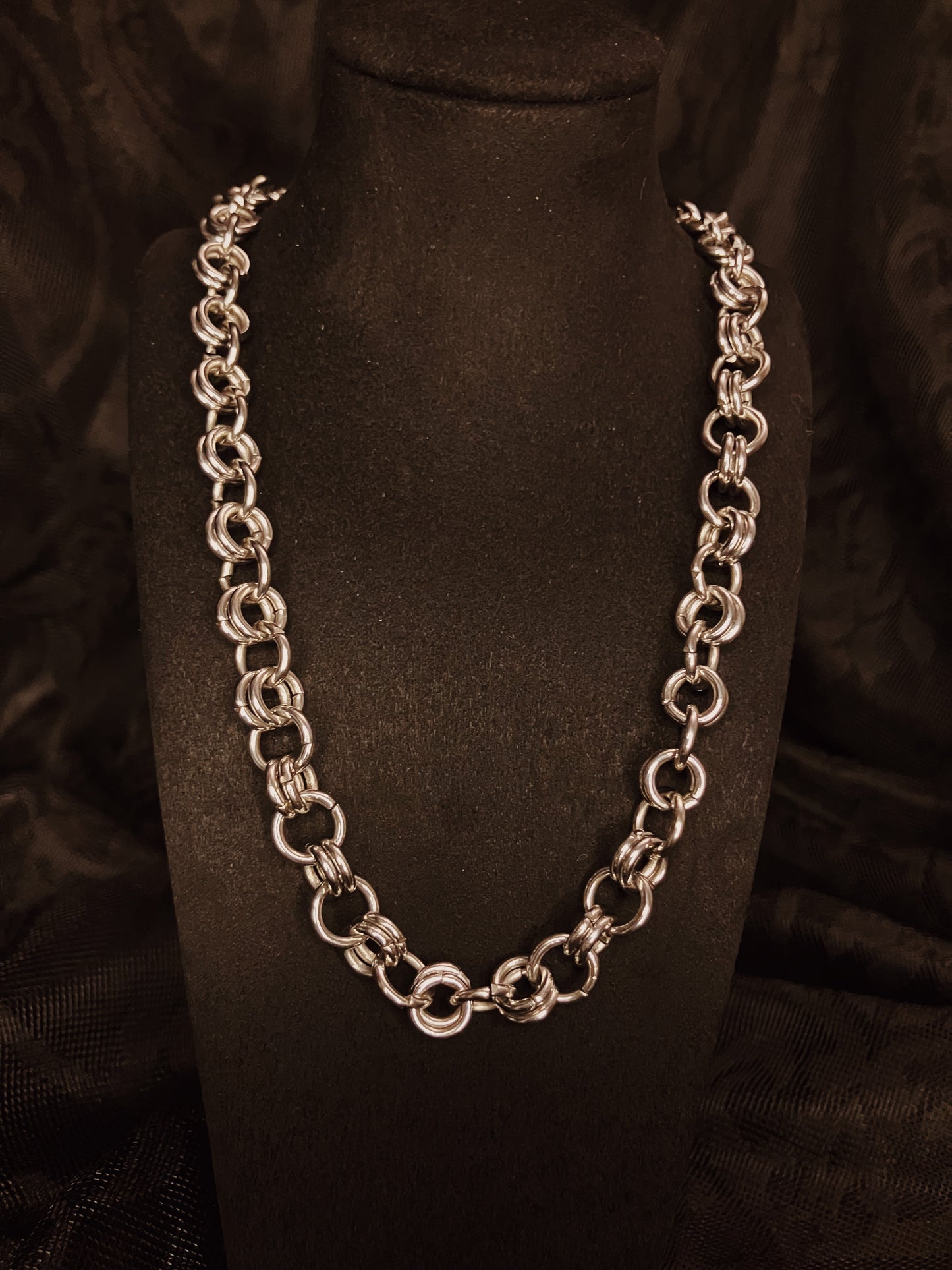 Silver chain necklace on a black mannequin bust against a dark background