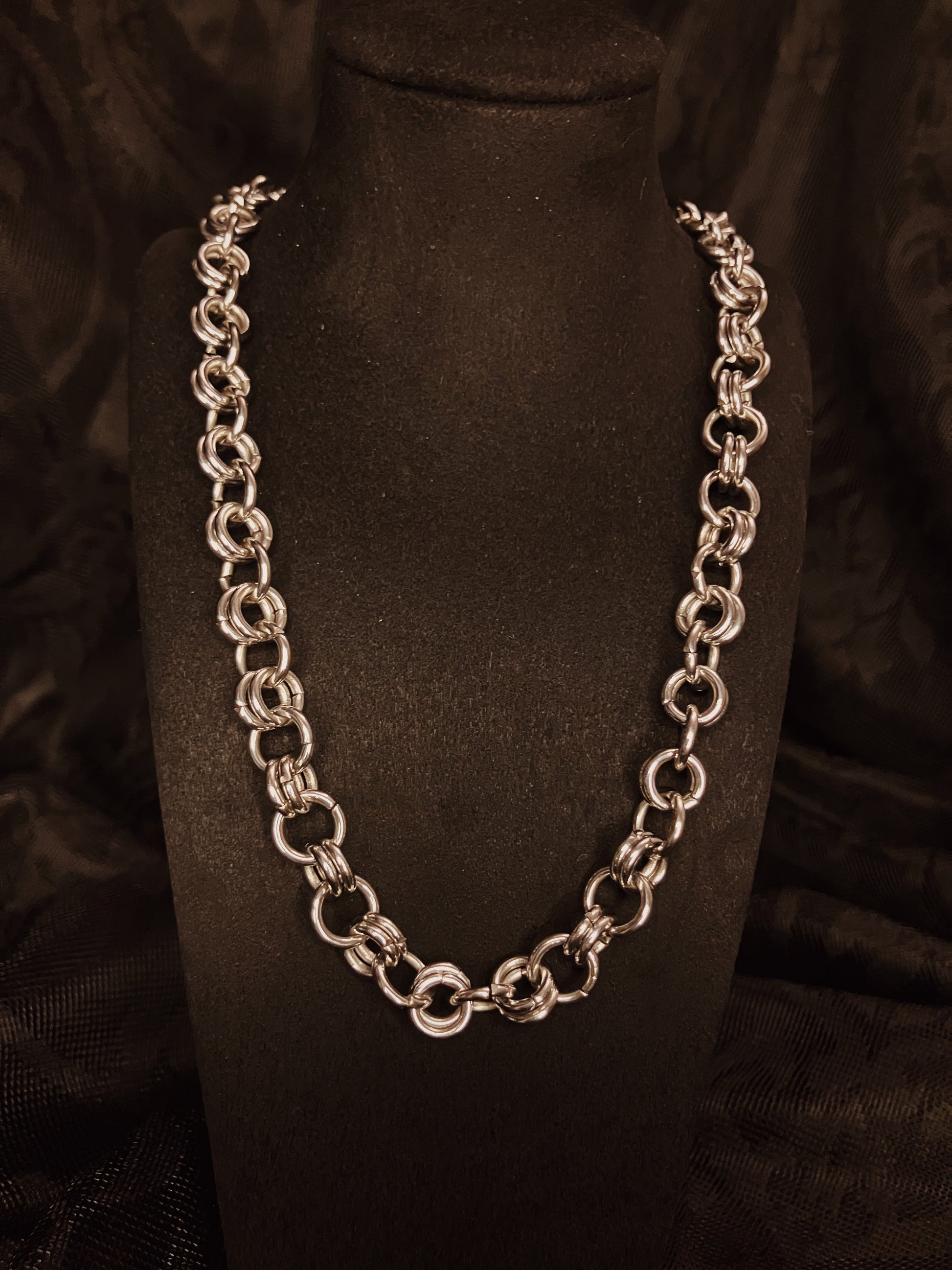 Silver chain necklace on a black mannequin bust against a dark background